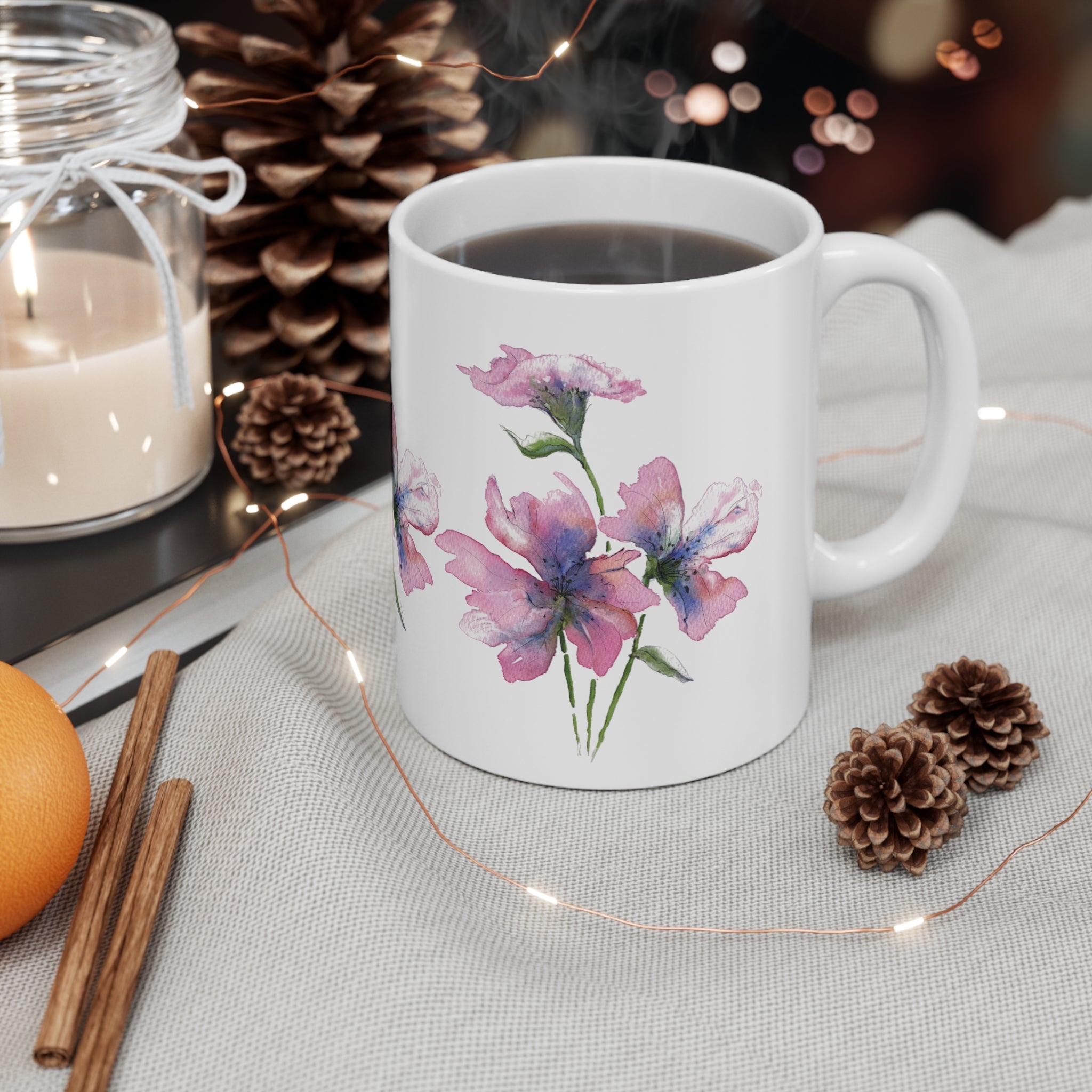 White mug with floral design on a table with candles, oranges, and pinecones.