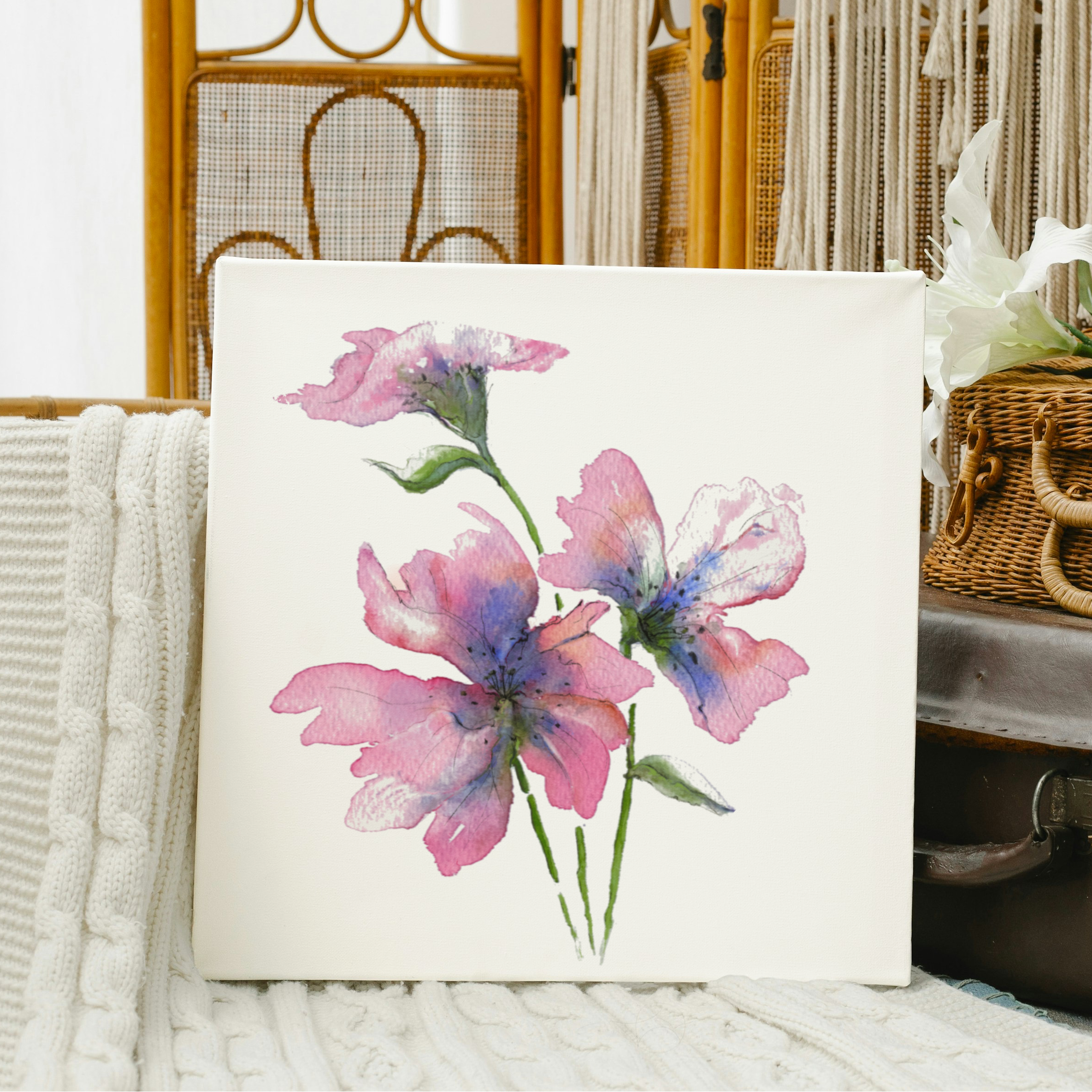 Floral painting on a white surface with a wicker basket and suitcase in the background.
