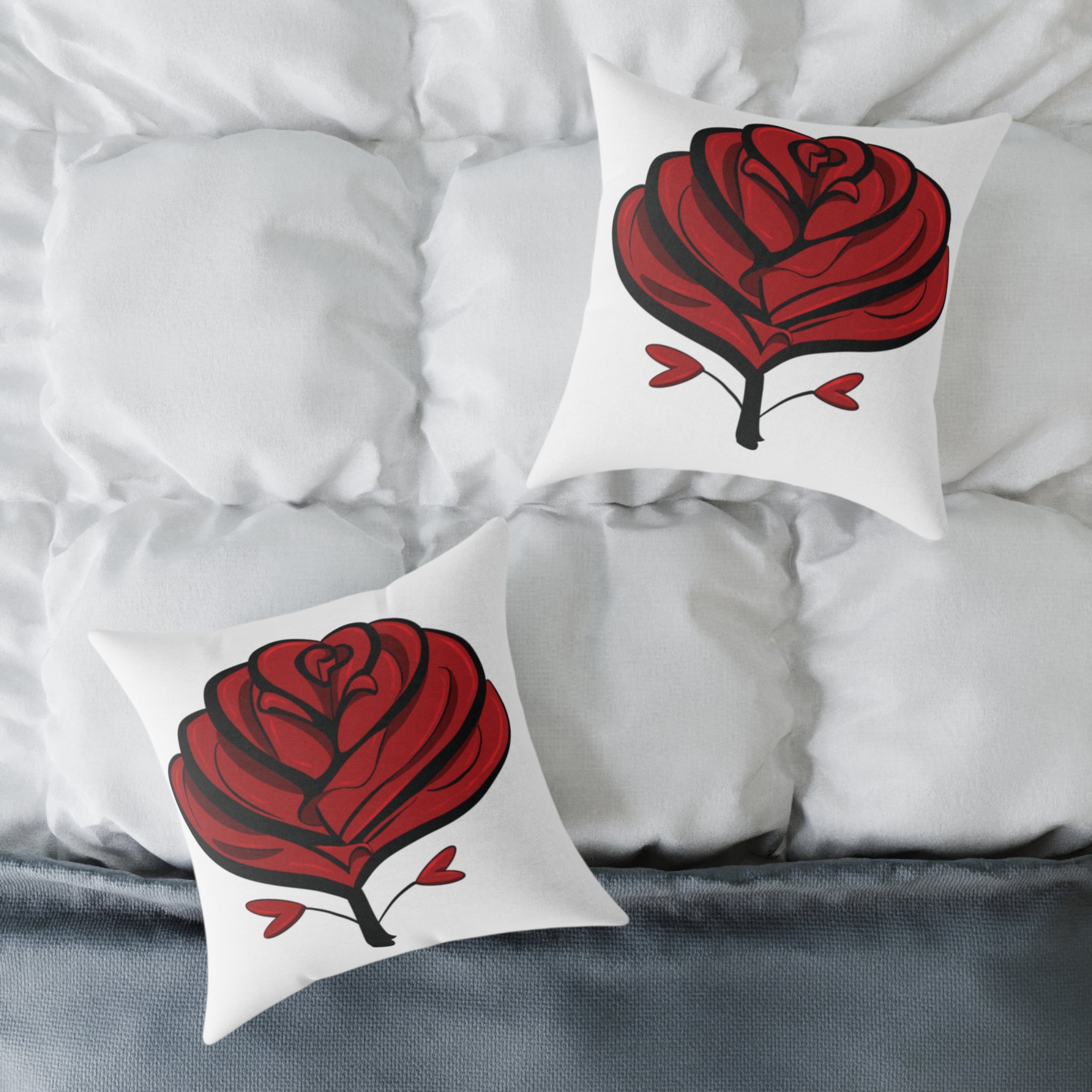 Two white pillows with red rose designs on a bed with white bedding.