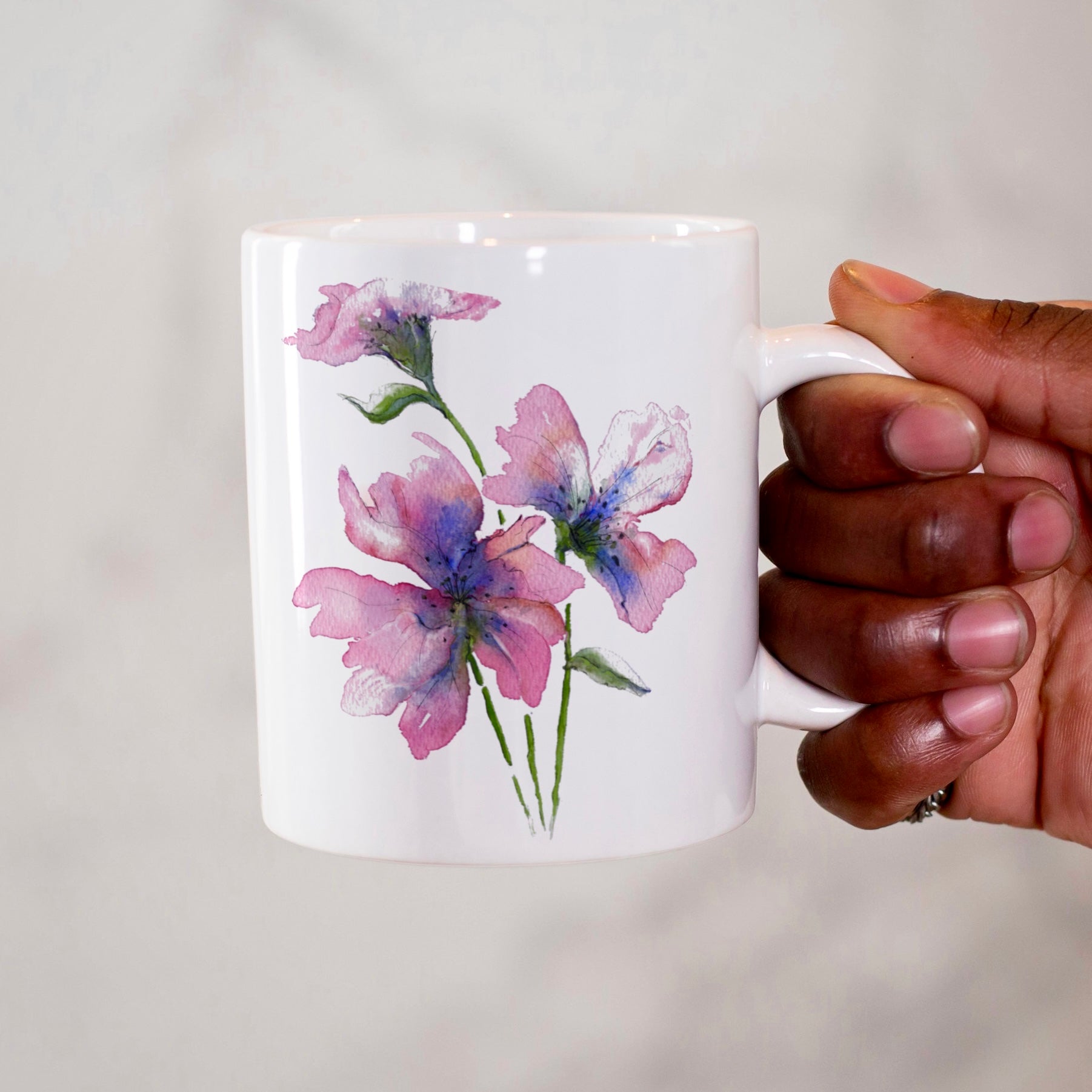 Hand holding a mug with floral design on a white background