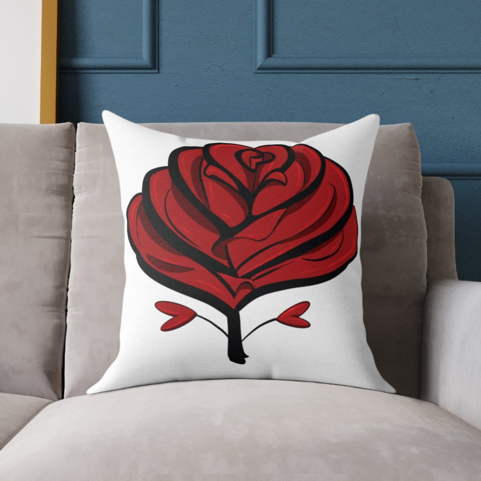 Decorative pillow with a red rose design on a gray sofa against a blue wall.