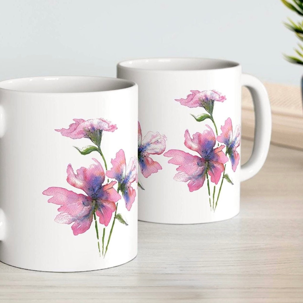 Two white mugs with floral designs on a light surface.