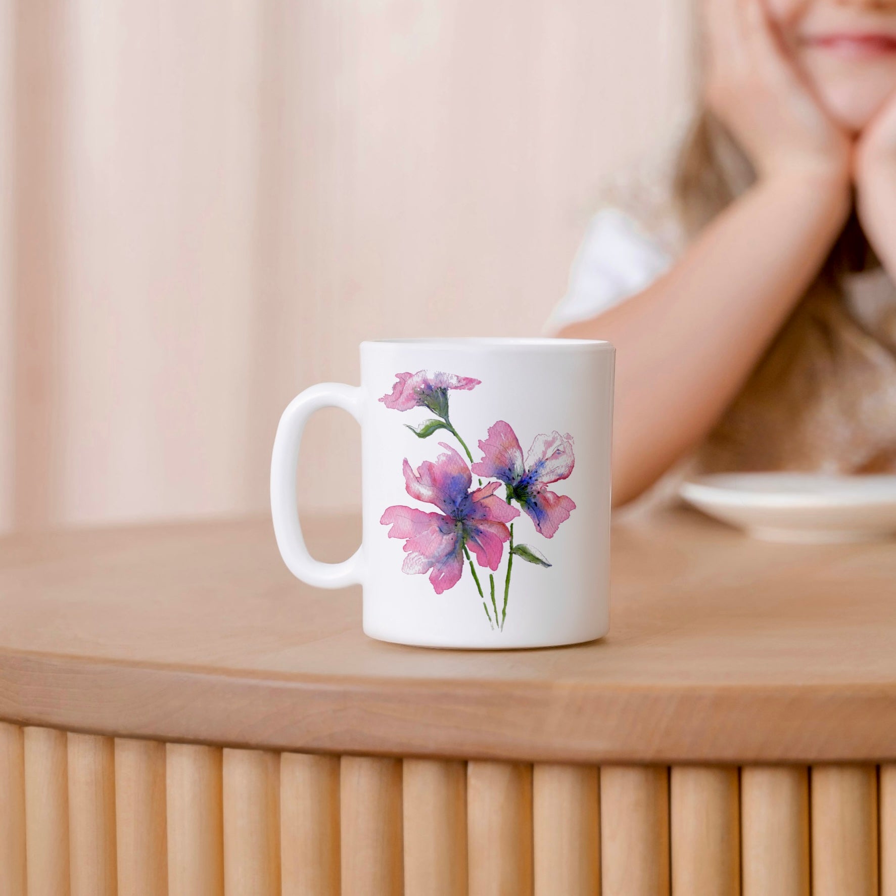 White mug with floral design on a wooden surface, blurred person in the background