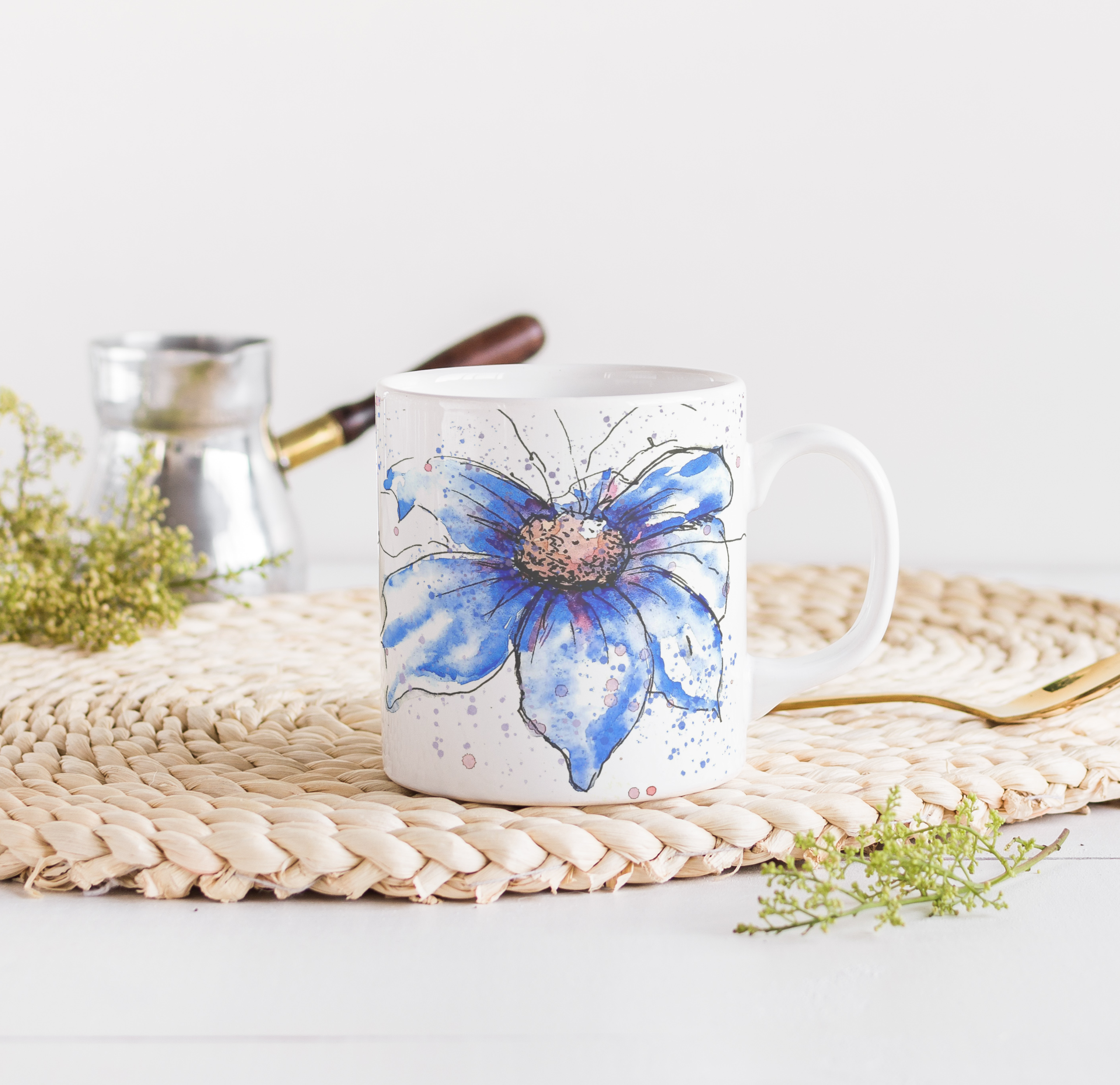 Blue cosmos watercolour mug on woven placemat with fresh greenery and natural morning light