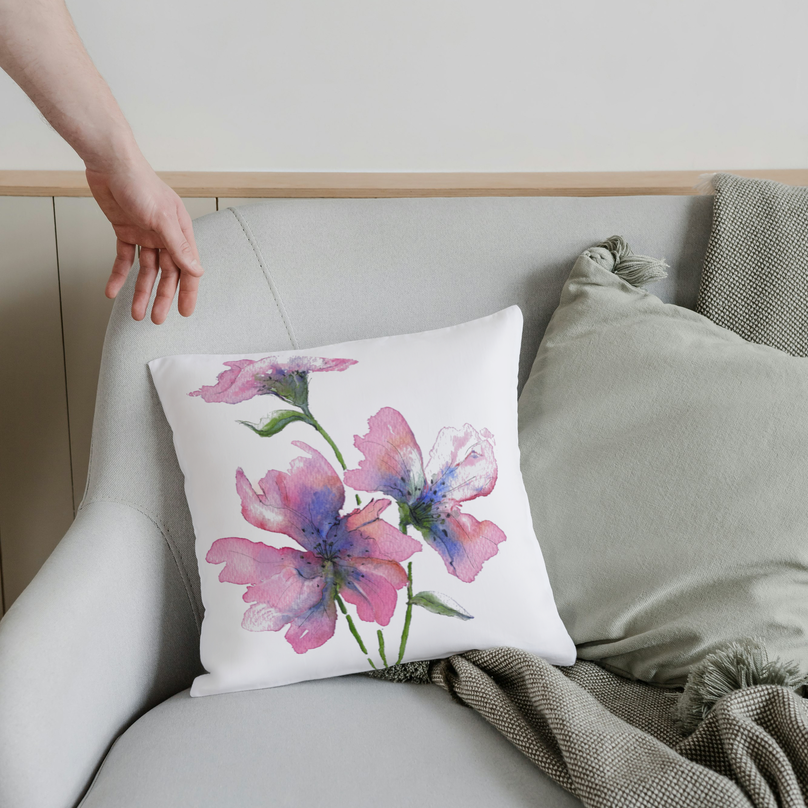 Floral pillow on a gray sofa with a person's hand reaching towards it.