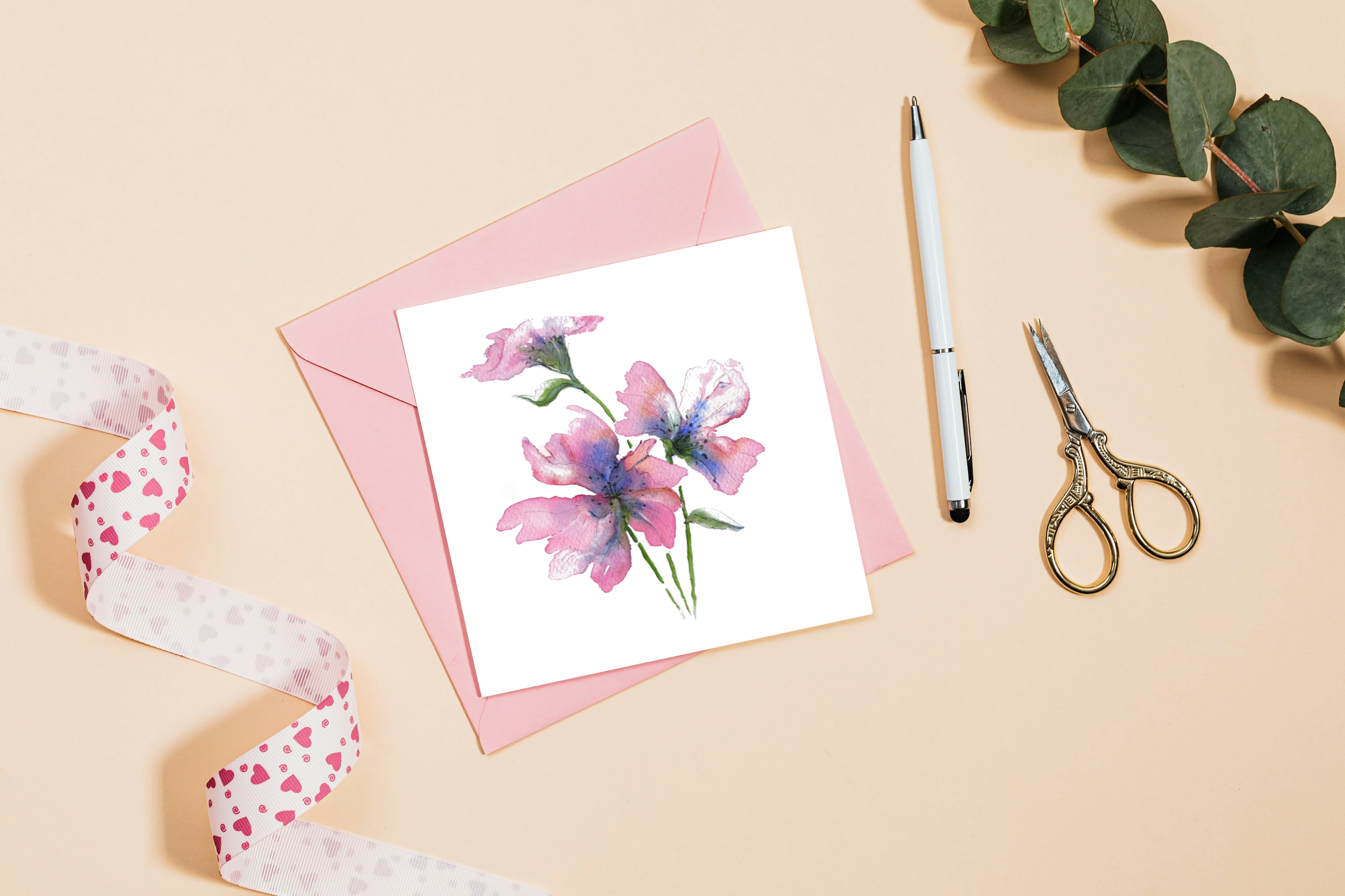Floral card with pink envelope, pen, and scissors on a beige background